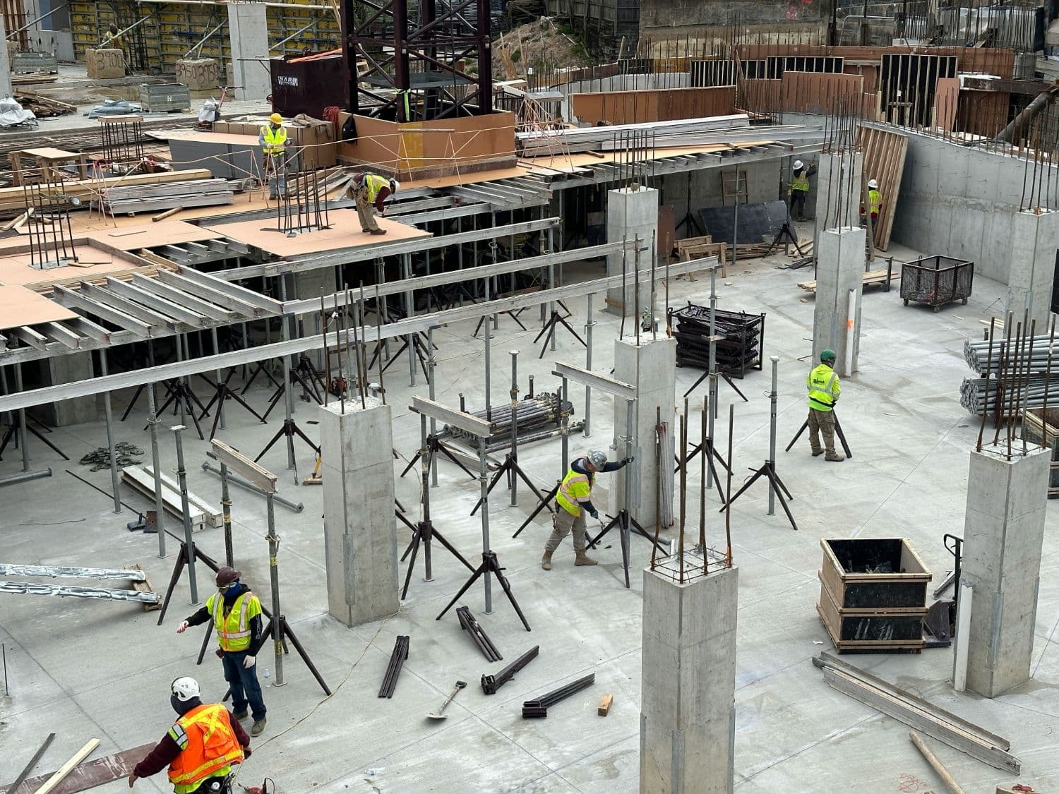 Crews working on a commercial new construction site with exposed rebar columns and shoring before walls go up