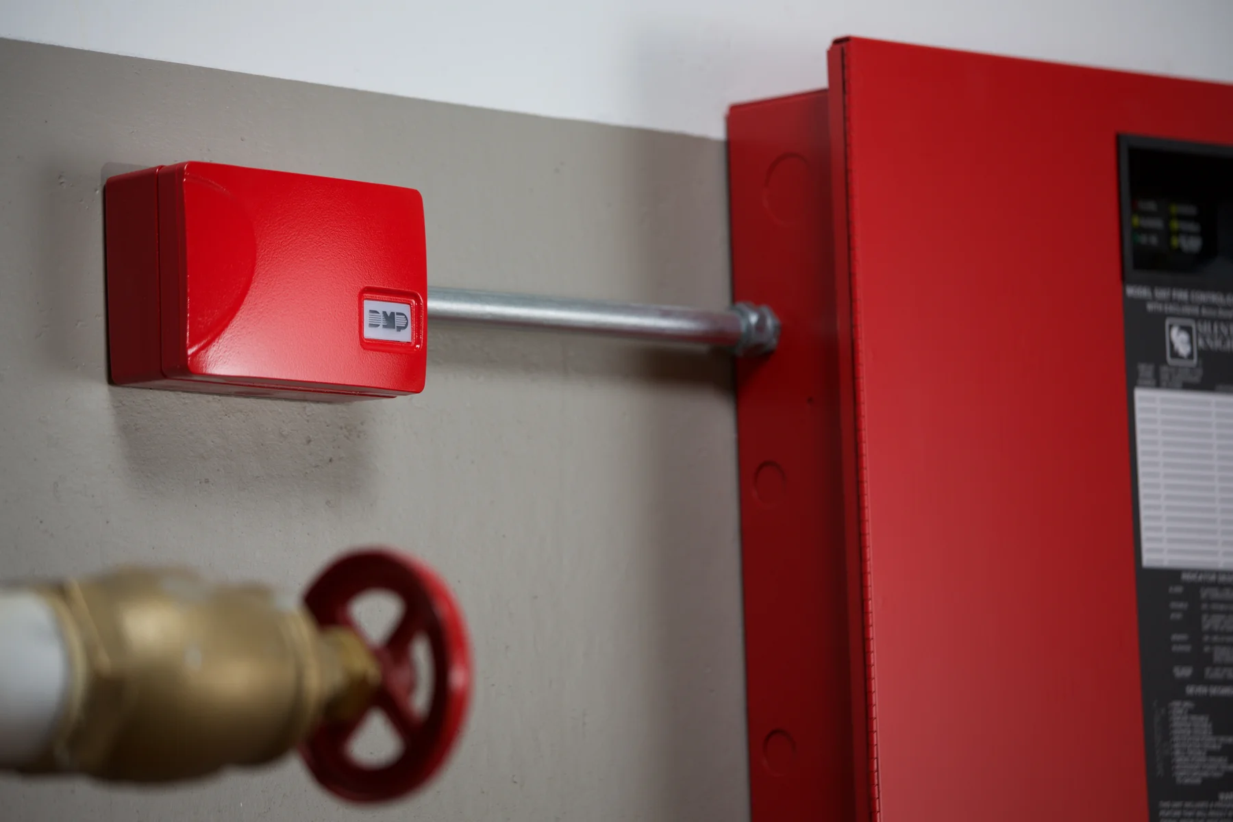 A red DMP communicator enclosure beside a fire alarm control panel