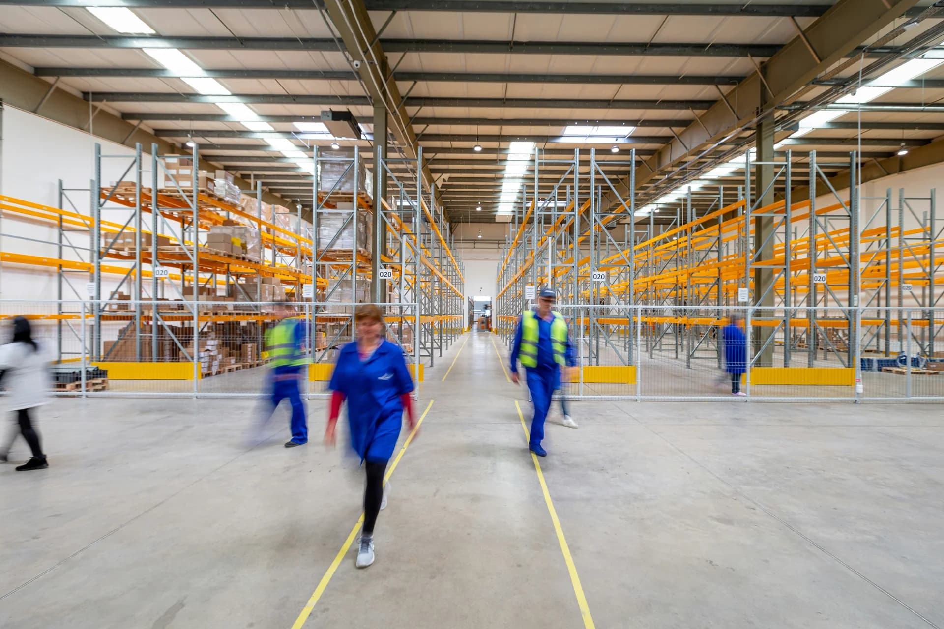 Employees walking through a warehouse with tall storage racks and a central aisle